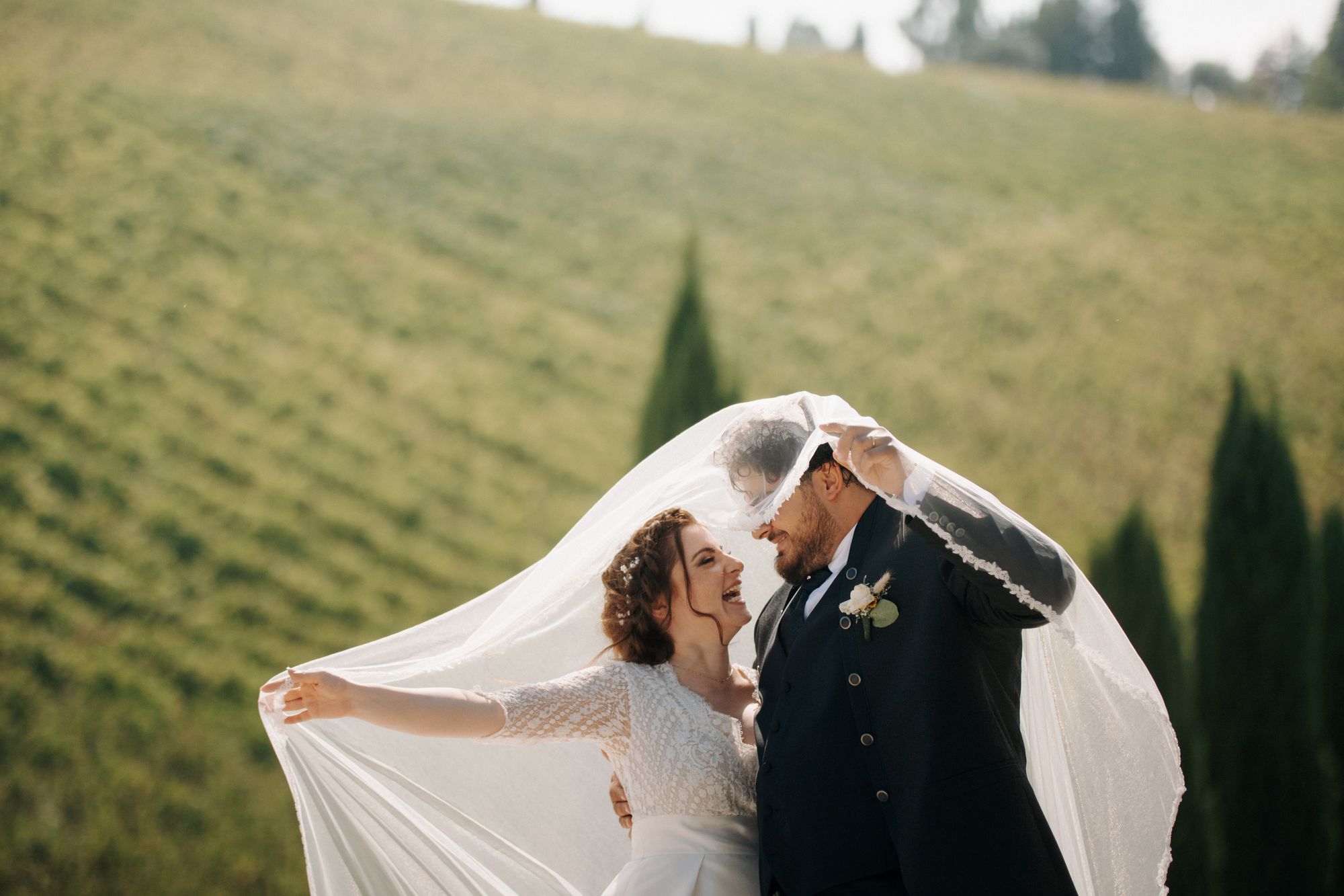 A couple kissing beneath a veil on a green hillside